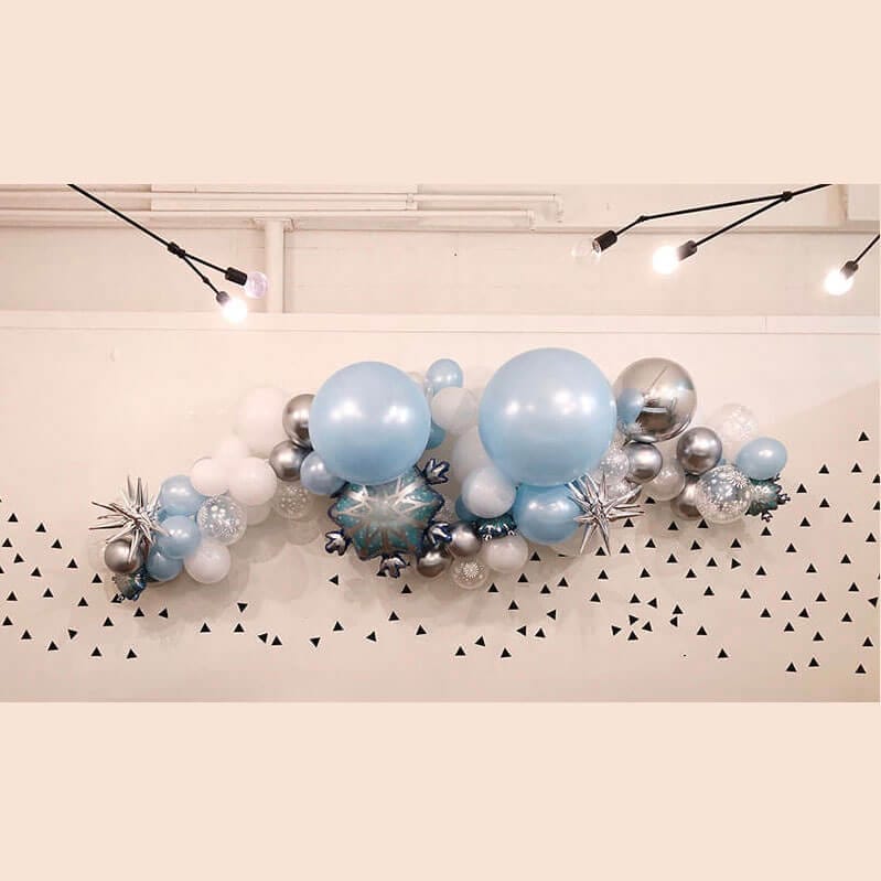 Pale blue, white, silver, and snowflake balloons make up this Frozen themed grab and go garland from Just Peachy.