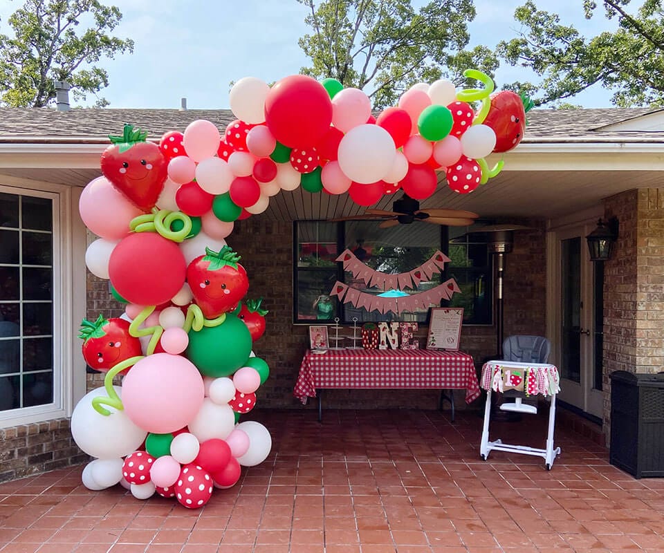 A strawberry balloon arch over the back patio entry for a first birthday party.