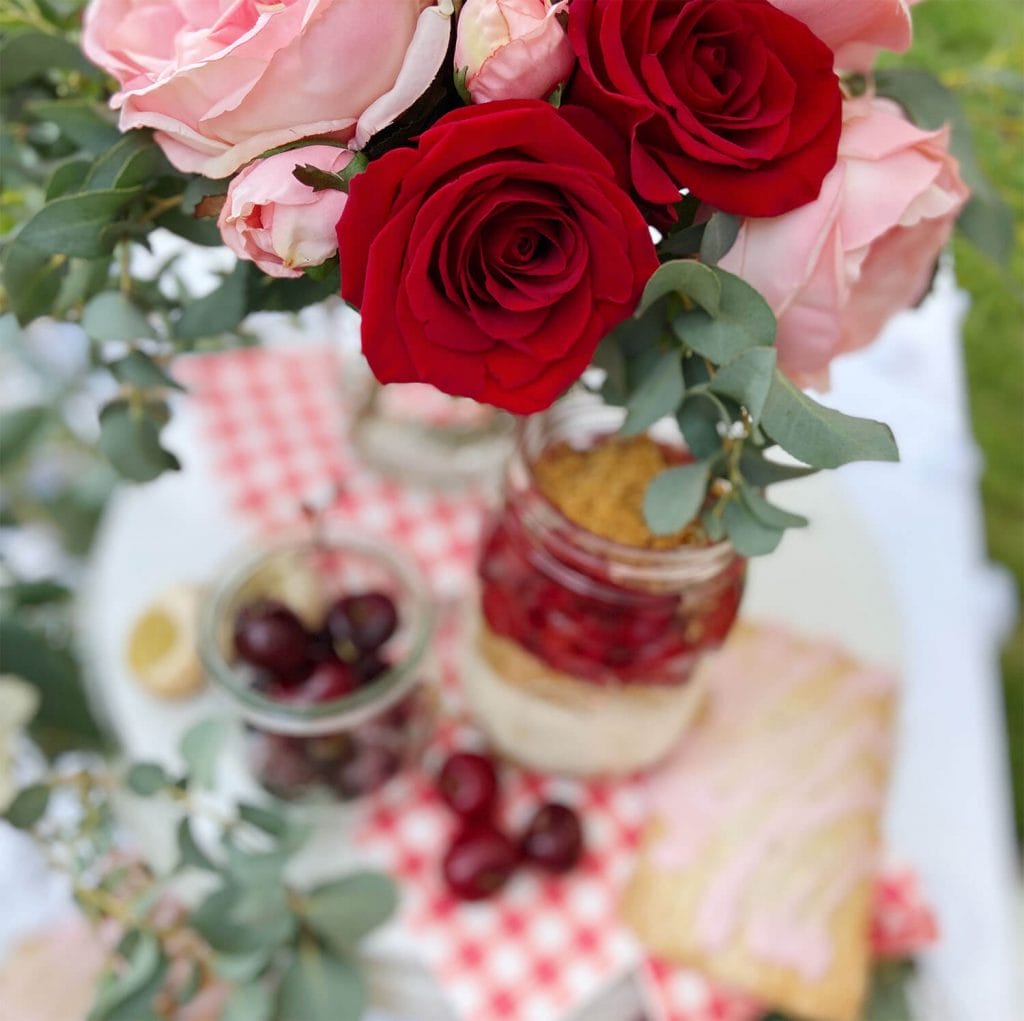 Red and pink roses on a red gingham tablecloth with cheesecake; party styled by Just Peachy.