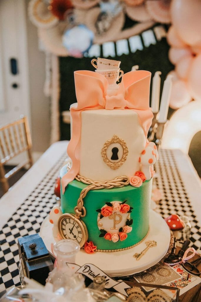 Two tier birthday cake in aqua and white with a pink bow, pocket watch and gold filigree details.