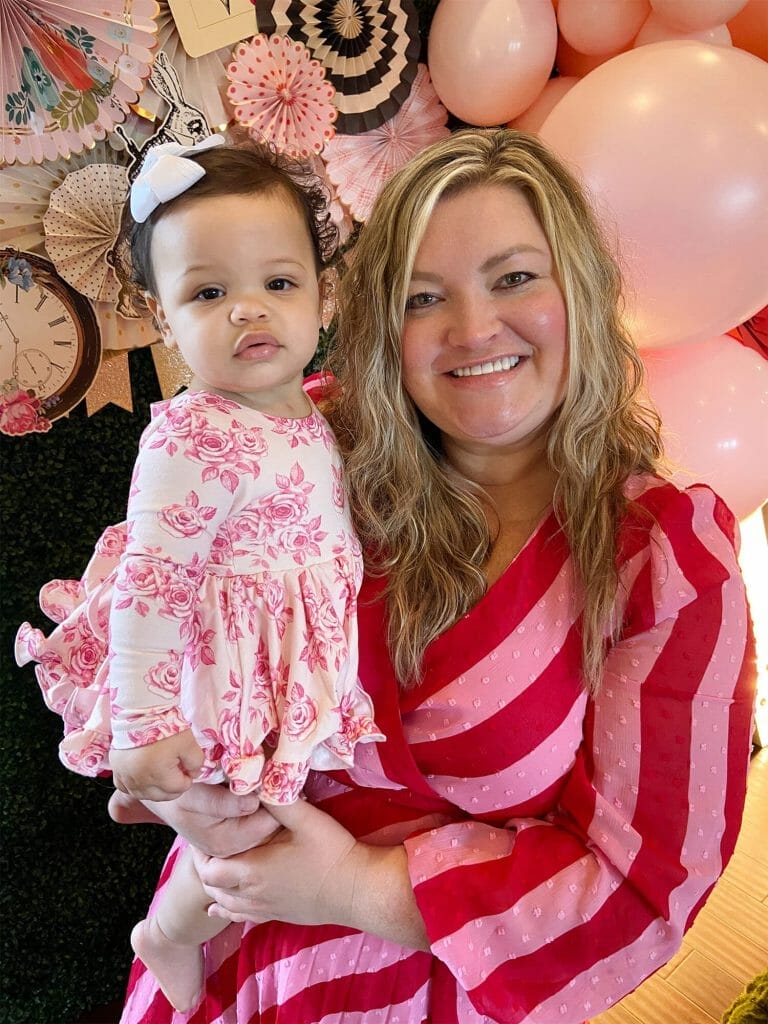 Baby and mom pose for a picture in red and pink Alice in Wonderland themed outfits.